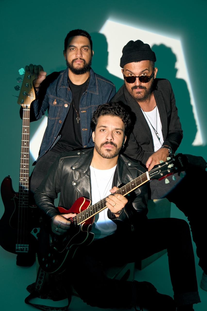 Trio reunido com guitarras sob luz verde-petróleo